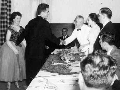 Robert com a mãe recebendo os cumprimento do pai na mesa diretora da cerimônia de formatura. Dezembro de 1956.
